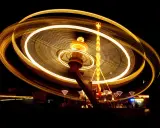 Effetto spirale di luci dorate su un'attrazione da luna park in movimento, catturata con una **panning shot** notturna.