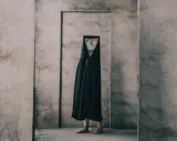 Figura con un orologio al posto della testa, avvolta in un drappo nero, in un ambiente spoglio. Un'opera che evoca i fotografi surrealisti contemporanei.
