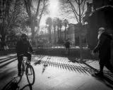 Ombre lunghe e un ciclista mascherato, in uno stile che ricorda robert doisneau, passeggiano sotto il sole.