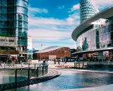 Un'area urbana moderna con grattacieli di vetro, un edificio curvo con il logo IBM e persone che passeggiano. Street photography esempi di vita cittadina.