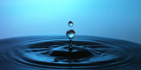 Momento magico nel fotografare gocce d'acqua: una cade, l'altra la segue, creando onde perfette su uno sfondo blu.