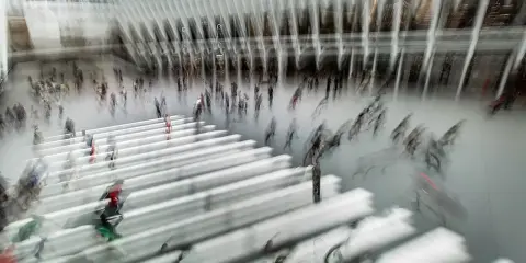 Persone in movimento in una grande hall moderna, con un forte effetto mosso che crea un senso di dinamismo e velocità.