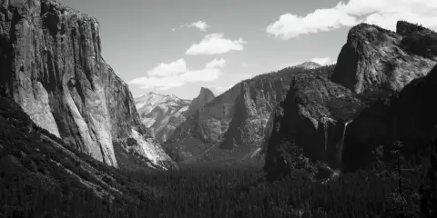 Iconici paesaggi di Yosemite, immortalati da fotografi famosi. Maestose pareti rocciose, una cascata e una fitta foresta sotto un cielo nuvoloso.