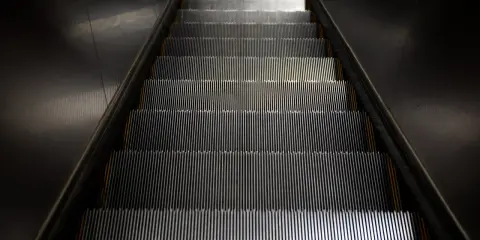 Scale mobili con un suggestivo **effetto moiré** creato dalle luci che si riflettono sui gradini metallici.