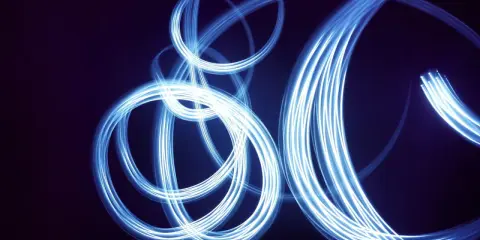 Light painting still life con fili di luce blu che danzano su sfondo scuro, creando un effetto etereo e astratto.