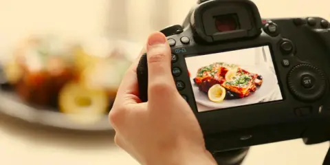 Mano che tiene una fotocamera per fare food photography di un piatto invitante con limone e erbe aromatiche.
