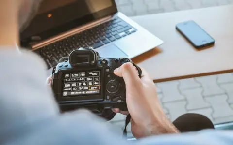 Una foto sera con una fotocamera reflex, un laptop e uno smartphone sul tavolo.