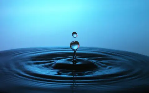 Momento magico nel fotografare gocce d'acqua: una cade, l'altra la segue, creando onde perfette su uno sfondo blu.