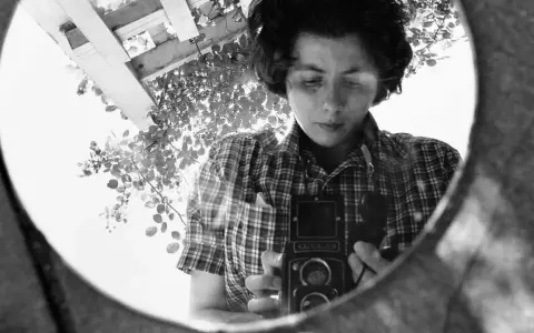 La fotografa famosa si riflette in uno specchio, impugnando la sua macchina fotografica.