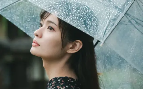 Una giovane donna con un ombrello trasparente osserva il cielo, la pioggia cade. Foto sotto la pioggia.