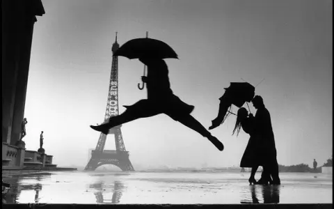 Parigi piovosa: un ballerino salta, una coppia si abbraccia sotto un ombrello. Un'iconica scena che ricorda i grandi fotografi famosi.