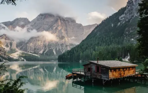Un rifugio di legno su un lago alpino, perfetto per fotografare paesaggi mozzafiato. Montagne imponenti e foreste verdi incorniciano la scena.