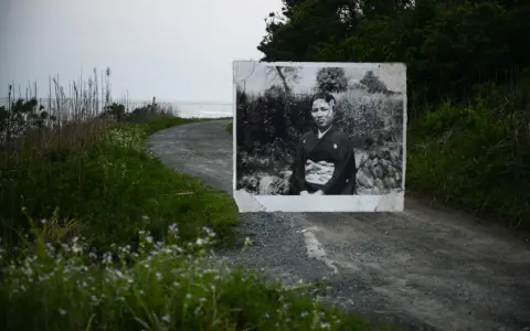 Un ritratto di una donna in kimono, evocativo dei fotografi giapponesi contemporanei, appare su una strada sterrata che conduce al mare.