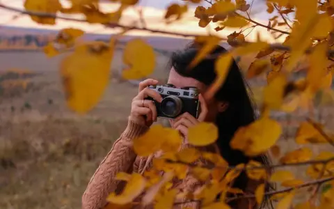 Ragazza con macchina fotografica vintage, tra foglie autunnali. Un tutorial fotografia per catturare la magia della natura.
