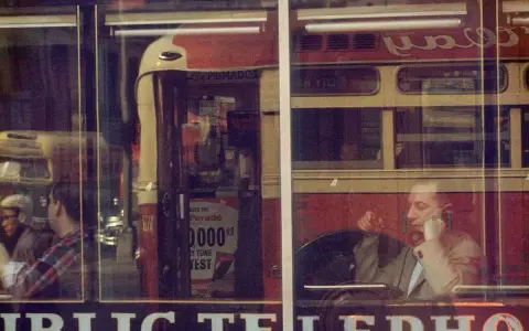 Un uomo al telefono, riflesso su una vetrina, evoca l'atmosfera urbana di Saul Leiter.