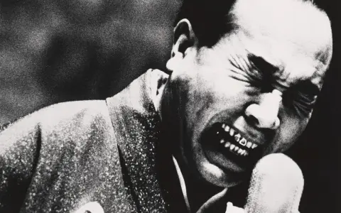 Un uomo con gli occhi chiusi e la bocca spalancata in un grido, un'espressione intensa catturata da Daidō Moriyama.