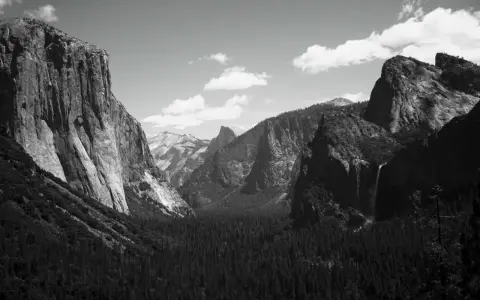 Iconici paesaggi di Yosemite, immortalati da fotografi famosi. Maestose pareti rocciose, una cascata e una fitta foresta sotto un cielo nuvoloso.