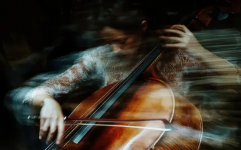 Donna suona il violoncello con un effetto mosso, quasi etereo. Un esempio di come fare foto mosse con iPhone per un risultato artistico.