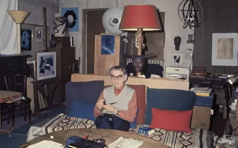 Man Ray nel suo studio, circondato da opere fotografiche e oggetti d'arte.