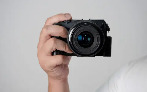 Mano che tiene una fotocamera compatta, mostrando le parti macchina fotografica come l'obiettivo e il corpo nero.