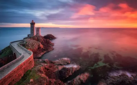 Faro su scogliera al tramonto, con cielo infuocato e mare calmo. Un filtro polarizzatore a cosa serve? A rendere i colori più vividi e il cielo più profondo.