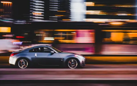 Auto sportiva grigia in movimento notturno, con luci sfocate sullo sfondo che creano un effetto di panning.