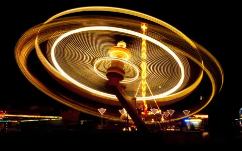Effetto spirale di luci dorate su un'attrazione da luna park in movimento, catturata con una **panning shot** notturna.