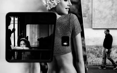 Un uomo cammina mentre una giovane donna guarda fuori da un finestrino. Un'immagine che evoca i grandi fotografi contemporanei.