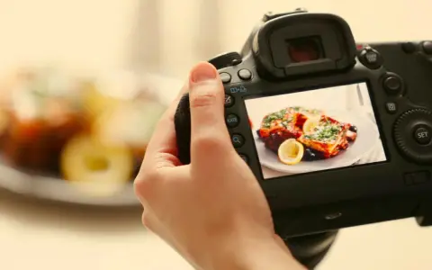 Mano che tiene una fotocamera per fare food photography di un piatto invitante con limone e erbe aromatiche.