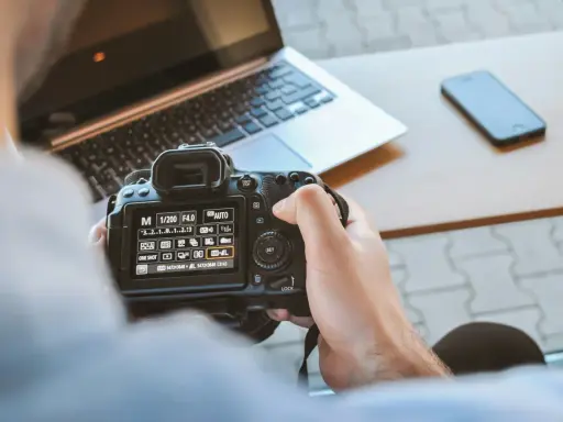 Una foto sera con una fotocamera reflex, un laptop e uno smartphone sul tavolo.