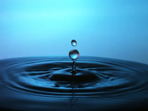 Momento magico nel fotografare gocce d'acqua: una cade, l'altra la segue, creando onde perfette su uno sfondo blu.