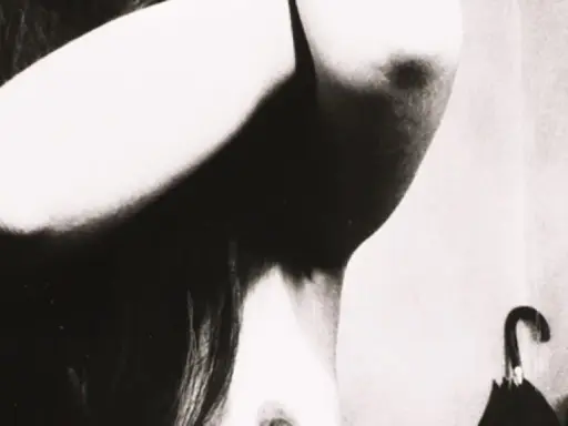 Un corpo femminile in primo piano, con le braccia sollevate, in uno stile che ricorda Bill Brandt. Un ombrello nero è appeso sullo sfondo.