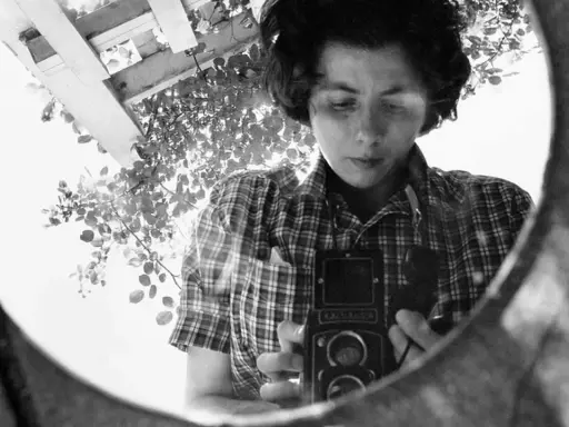 La fotografa famosa si riflette in uno specchio, impugnando la sua macchina fotografica.
