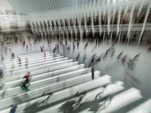 Persone in movimento in una grande hall moderna, con un forte effetto mosso che crea un senso di dinamismo e velocità.