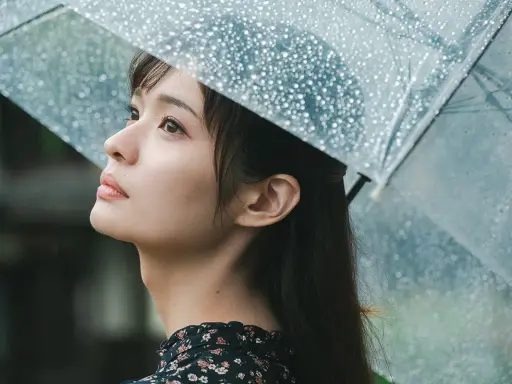 Una giovane donna con un ombrello trasparente osserva il cielo, la pioggia cade. Foto sotto la pioggia.