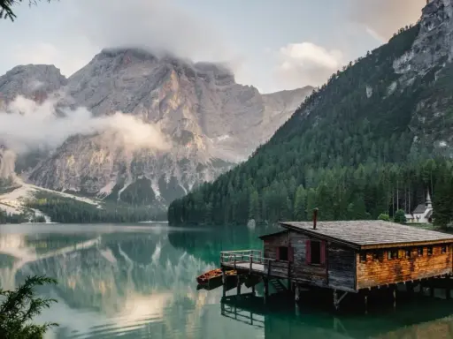 Un rifugio di legno su un lago alpino, perfetto per fotografare paesaggi mozzafiato. Montagne imponenti e foreste verdi incorniciano la scena.