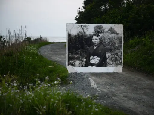 Un ritratto di una donna in kimono, evocativo dei fotografi giapponesi contemporanei, appare su una strada sterrata che conduce al mare.