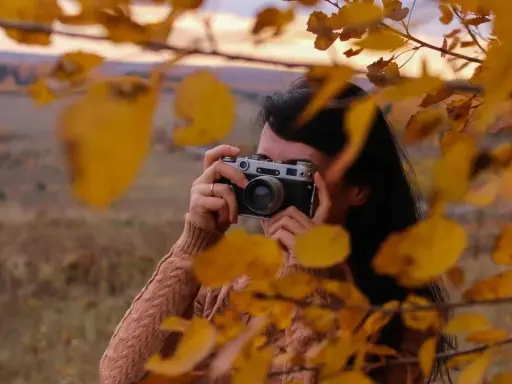 Ragazza con macchina fotografica vintage, tra foglie autunnali. Un tutorial fotografia per catturare la magia della natura.