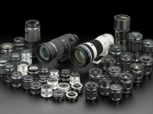 Una vasta collezione di obiettivi fotografici, dai più compatti ai teleobiettivi professionali, disposti su sfondo nero.
