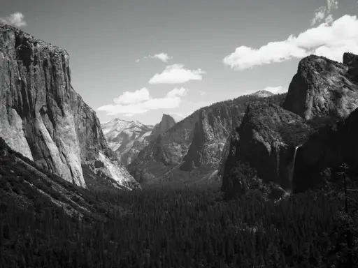 Iconici paesaggi di Yosemite, immortalati da fotografi famosi. Maestose pareti rocciose, una cascata e una fitta foresta sotto un cielo nuvoloso.