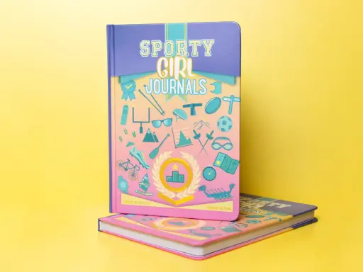 Come fotografare un libro: due quaderni "Sporty Girl Journals" con copertine colorate e illustrazioni sportive su sfondo giallo.