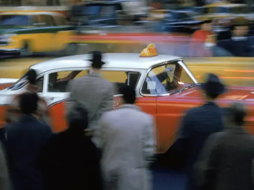Un taxi rosso e bianco sfreccia in una strada trafficata, un'istantanea che cattura l'essenza di quando nasce la fotografia a colori.
