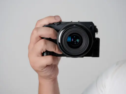 Mano che tiene una fotocamera compatta, mostrando le parti macchina fotografica come l'obiettivo e il corpo nero.