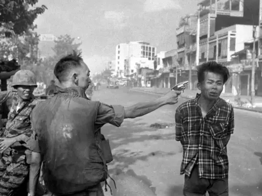 Un soldato punta una pistola alla testa di un uomo in un crudo reportage di guerra. La scena è ambientata in una strada urbana.