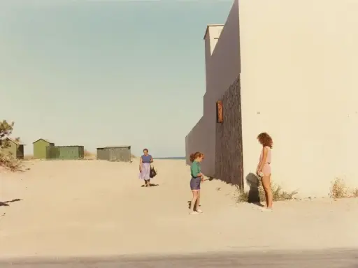 Ghirri fotografo cattura un momento estivo: due bambine e una donna sulla spiaggia, con capanne verdi sullo sfondo e un muro bianco imponente.