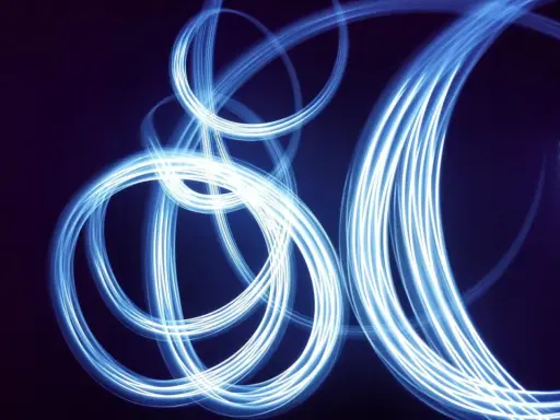 Light painting still life con fili di luce blu che danzano su sfondo scuro, creando un effetto etereo e astratto.