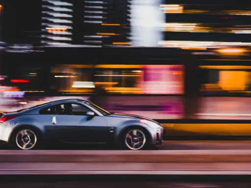 Auto sportiva grigia in movimento notturno, con luci sfocate sullo sfondo che creano un effetto di panning.