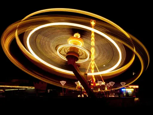 Effetto spirale di luci dorate su un'attrazione da luna park in movimento, catturata con una **panning shot** notturna.