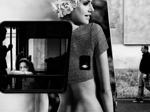 Un uomo cammina mentre una giovane donna guarda fuori da un finestrino. Un'immagine che evoca i grandi fotografi contemporanei.