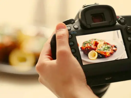 Mano che tiene una fotocamera per fare food photography di un piatto invitante con limone e erbe aromatiche.